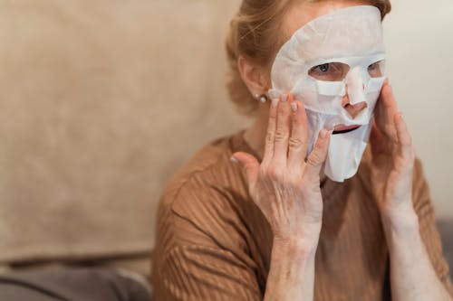 A woman over 60 applying a hydrating sheet mask at home